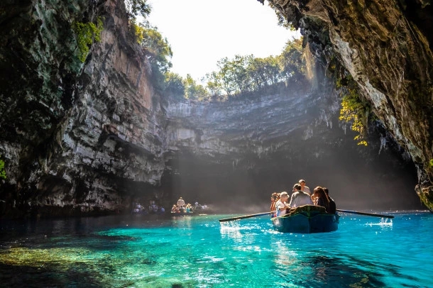 Sunlight falling into a cave above vivid blue water and a small boat